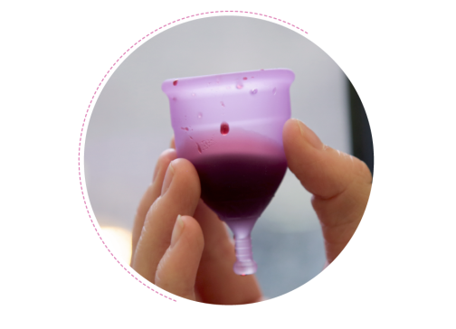 A hand holds a menstrual cup that is filled with blood